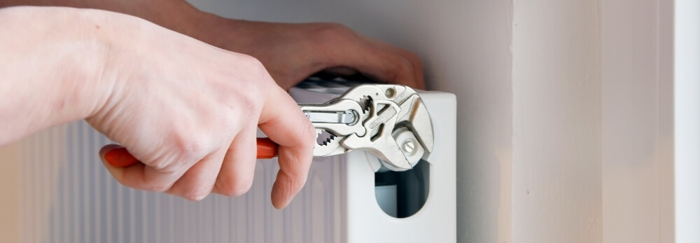 Person repariert Heizkörper mit Rohrzange